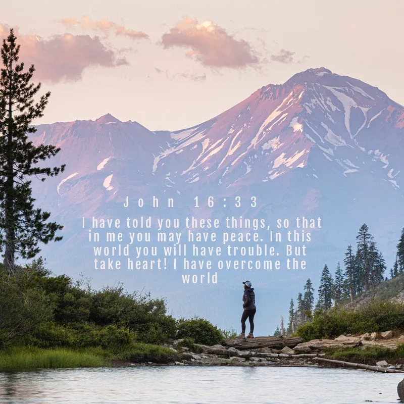 John 16:33 over a hiker facing a snowy mountain at sunset